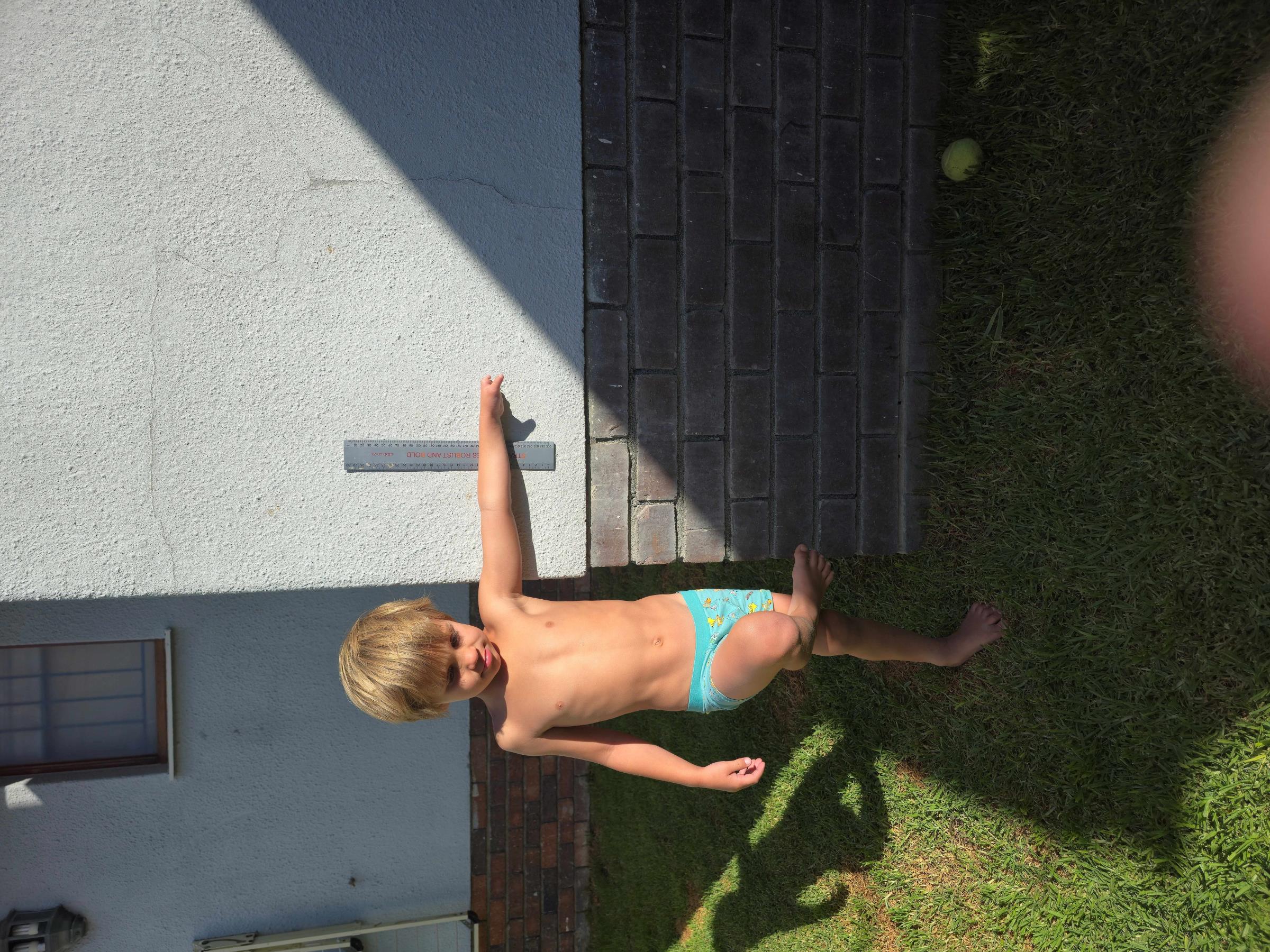 Noah arms outstretched outside against a white wall, showing the full span of both arms